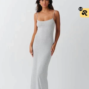 Ljusgrå långklänning med smala axelband - Supersnygg ljusgrå långklänning med smala axelband och figurnära passform. Enkel och stilren design som ger en clean look. Perfekt för dig som gillar minimalistiskt mode och vill ha något bekvämt men ändå trendigt.