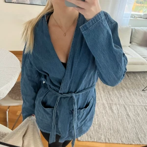 Blå jeansjacka med bälte från Zara - Blå jeansjacka, kofta i bomull från Zara med knytning i midjan och stora fickor framtill. Passar xs / s