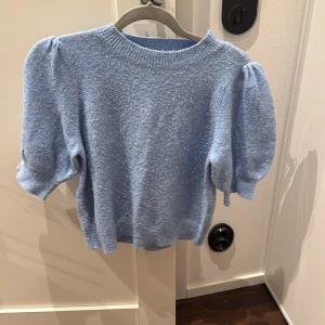 Ljusblå stickad tröja med puffärm - Superfin ljusblå stickad tröja med korta puffärmar och rund halsringning. Mjuk och skön, perfekt för vår eller sommarkvällar. Enkel att styla till både jeans och kjol för en söt look.