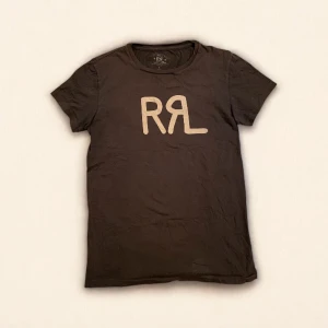 Svart t-shirt från Ralph Lauren RRL - Tjena! Säljer denna sjukt snygga Double RL tishan då den tyvärr inte passade min storlek.  Den är i superfint skick och har inget att anmärka på. Den ser brunaktig ut på annonsen men är i själva verket mörkgrå/svart, fråga gärna om bild så kan jag försöka fixa tydligare!  Har ni bud eller frågor är det bara att höra av er :)