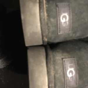 Svarta UGG boots med rosett-köparen står för frakten  - Mysiga svarta UGG boots i mocka med fluffigt foder och dekorativa rosetter baktill. Klassisk rund tå och platt sula, perfekta för kalla dagar. UGG-logga på hälen och snygg enkel design som passar till många outfits.