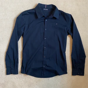 Tommy Hilfiger skjorta, storlek 176 - Marinblå Tommy Hilfiger skjorta i bomull. Endast använd ett fåtal gånger så i princip nyskick. Priset går att diskutera!