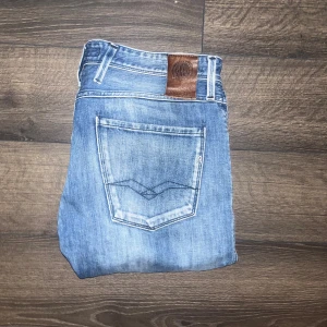 Replay Anbass jeans - Säljer ett par Replay Anbass jeans i ljusblå tvätt med snygga slitningar och klassiska bakfickor. Jeansen har slim passform. OBS som det syns finns det ett hål på ena knäet som jag ej vet om det är defekt heller styling, och en pytteliten slitning på andra benet. Midja 43cm, längd 111cm. JAG SKICKAR EJ FLER BILDER NÄR JAG BÄR JEANSEN! för storleksguide hänvisar jag till måtten och för bättre inblick i passformen rekommenderar jag att googla på modellnamnet :) s3