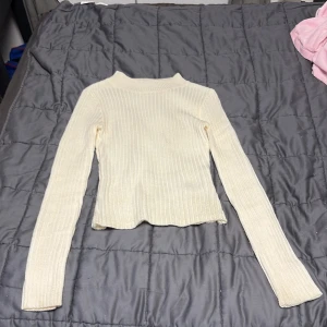 Ribbad vit stickad tröja H&M Divided XS - Ribbad vit stickad tröja från H&M Divided i storlek XS. Tröjan har lång ärm, högre hals och en slim passform. Perfekt att styla med jeans eller kjol för en clean look.