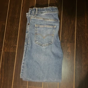 Levi's 501 blå raka jeans - Klassiska Levi's 501 jeans i ljusblå denim med raka ben och normal passform. Jeansen har fem fickor, gylf med knappar och ikonisk läderpatch bak i midjan. Perfekta för en avslappnad och tidlös look.