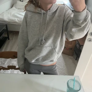 Grå hoodie med huva och ficka - Säljer en ljusgrå hoodie med huva och snörning. Tröjan har en stor magficka och ribbade muddar vid ärmslut och nederkant. Passformen är loose och den är perfekt för chill dagar. Materialet känns mjukt och skönt mot huden.