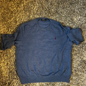 Blå stickad tröja från Polo Ralph Lauren - Snygg blå stickad tröja från Polo Ralph Lauren i storlek XL. Tröjan har rund hals, långa ärmar och den klassiska röda broderade loggan på bröstet. Perfekt för dig som gillar stilrena och tidlösa plagg med premiumkänsla.