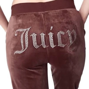 Bruna Juicy Couture mjukisbyxor - Bruna mjukisbyxor från Juicy Couture med glittrande strassdetaljer som bildar texten 'Juicy' över baken. Byxorna har bred resår i midjan och är gjorda i mjuk sammet för en skön och lyxig känsla.