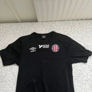 Svart Angered Allians fotbollströja - Säljer en svart fotbollströja från Umbro i storlek M med Angered Allians klubbmärke på bröstet. Materialet är lätt och andas, perfekt för träning eller match.