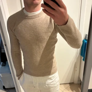 Beige stickad tröja These Glory Days - Säljer en stilren beige stickad tröja från These Glory Days. Tröjan har rund halsringning, ribbade muddar och är långärmad. Perfekt för lager-på-lager och passar till allt. Materialet är mjukt och skönt, perfekt för kyligare dagar. Sitter som xs/xxs