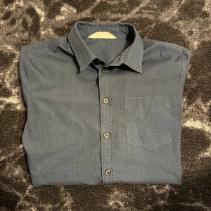 Mörkblå klassisk skjorta i bomull - Snygg mörkblå skjorta med klassisk krage och bröstficka. Skjortan har långa ärmar med manschett och knappar hela vägen framtill. Tillverkad i mjuk bomull som känns skön mot huden. Perfekt för dig som gillar en clean och stilren look.