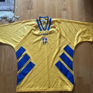 Sverige Landslagströja 1990/91 – Adidas – XL – Retro / Vintage - Säljer en äkt vintage Sverige-tröja från tidigt 90-tal — Adidas original i storlek XL.  Detta är samma modell som bars i perioden precis före EM 1992, och är idag ett riktigt samlarobjekt. Tröjan har den klassiska designen med vävt mönster av SFF-emblem, samt de blå diagonala blocken på sidorna – en av de mest ikoniska Sverige-tröjorna någonsin.
