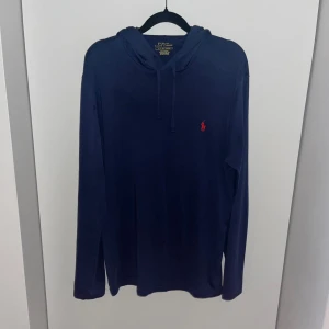 Ralph Lauren hoodie - Snygg marinblå hoodie från Polo Ralph Lauren med klassisk röd logga broderad på bröstet. Tröjan har huva med snörning och långa ärmar. Tillverkad i mjuk bomull som känns skön mot huden. Axelbredd 44cm, längd 69cm. fall det inte finns någon bild i annonsen där jag bär plaggen jag säljer så är det för att jag ej kan ha storleken heller passformen, så kolla måtten för storlek och googla på modellnamnet för passform 😉25