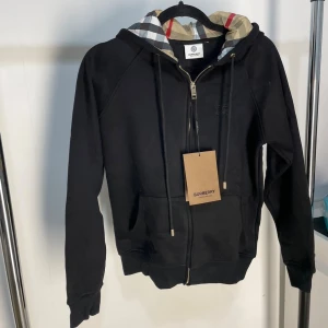 Svart Burberry hoodie med dragkedja - Svart hoodie från Burberry. Perfekt för dig som gillar stilrena och lyxiga plagg. En fin tröja inför hösten/vintern.