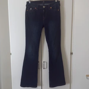 Mörkblå true religon - Snygga mörkblå true religon jeans i modellen Becca  med bootcut-modell som sitter tajt upptill och släpper ut vid benen. Klassisk femficksdesign och midja som sitter perfekt. Perfekta för dig som gillar en tidlös och trendig look. Är upplagda lite (går att sprätta upp det igen) jag är 167 med långa ben så dom sitter perfekt på mig. Har lite slitningar längst ner i kanten men inget som syns.