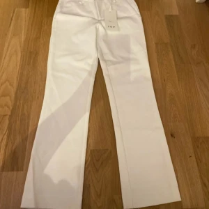Vita kostymbyxor från IVY, stl 24/28 - Snygga vita kostymbyxor från IVY med raka ben och klassisk passform. Byxorna har hällor för bälte, knapp och dragkedja framtill samt diskreta bakfickor. Perfekta för en clean och stilren look. Materialet är slätt och känns lyxigt.