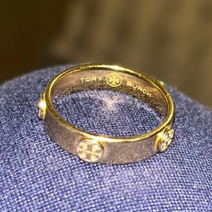  Tory Burch ring - Sälj min guld ring från TORY BURCH som inte kommer till användning. Köpt på ZALANDO. Den är i rostfritt stål så man kan duscha och tvätta händerna med den.  Så nypris ligger på ca 1.500kr.  I storlek 7 som motsvarar även 54 och 17! Dustbag medföljer! Fått ringen i present.  Inga skador eller synliga repor som jag kan se.