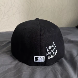 Svart New Era Yankees keps 59FIFTY - Snygg svart New Era 59FIFTY keps med broderad Yankees-logga i vitt och ett litet hjärta på framsidan. Texten 'Love Hustle Game' är broderad på sidan. Klassisk rak skärm och broderade detaljer. Perfekt för dig som gillar streetstyle och sport.