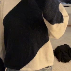 Mysig svartvit stickad tröja - Säljer en  stickad tröja i mörkblått och vitt med breda diagonala blockmönster. Tröjan har rund halsringning och långa ärmar, perfekt för kyliga dagar. Passar dig som gillar en avslappnad och trendig stil.