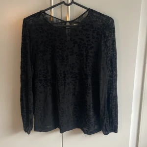 Svart meshblus med leopardmönster 365 - Säljer en svart meshblus från 365 i storlek M. Blusen har ett diskret leopardmönster i sammet, långärmad modell och rund halsringning. Tunt och lätt material som ger en cool look med transparenta partier och en liten knappdetalj i nacken.
