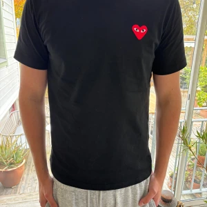 Svart Comme des Garçons t-shirt - Svart t-shirt från Comme des Garçons Play med det ikoniska röda hjärtat med ögon broderat på bröstet. Klassisk passform, rund hals och korta ärmar. Tillverkad i mjuk bomull som är skön mot huden. Tröjan är självklart äkta och ändats använd 1 gång. Modellen på bilderna är 180cm lång och väger ca 70kg