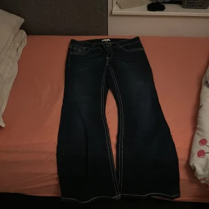 Mörkblå bootcut jeans från Gina Tricot - Snygga mörkblå jeans från Gina Tricot i bootcut-modell med kontrasterande vita sömmar. Klassisk femficksdesign och detaljerade bakfickor med lock och knapp. Jeansen har normal passform och är tillverkade i jeansmaterial.