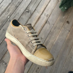Lanvin beige sneakers med mocka och gummitå - Lanvin sneakers i beige mocka med rund gul gummitå och platt vit sula. Klassisk låg modell med snörning och metallöglor. Snygg kontrast mellan mocka och gummi framtill, perfekt för dig som gillar stilrena och unika detaljer.