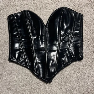 Svart glansig korsett med snörning XXS - Säljer en svart glansig korsett i storlek XXS med snygga sömmar och snörning baktill. Materialet är polyester och polyamid med en blank yta av polyuretan. 