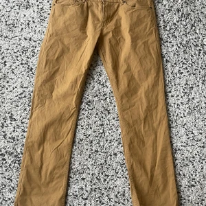 Beiga chinos från Hampton Republic W34 L32 - Snabb leverans. Snygga beiga chinos från Hampton Republic i storlek W34 L32. Byxorna är tillverkade i 98% bomull och 2% elastan för en skön passform. Klassisk rak modell med fickor fram och bak, perfekta för en clean och stilren look.