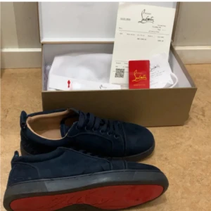 Mörkblå sneakers från Louboutin - Säljer ett par mörkblå sneakers från Christian Louboutin i mocka med klassisk röd sula. Skorna har snörning, rund tå och en stilren design som passar perfekt till streetwear. Kommer med originalkartong och dustbag.