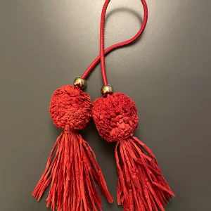 Röd Väskdekoration  - En stark röd dekoration till väskan för att piffa upp den lite! Man kan knyta den runt remmen på väskan 💕köpt nyligen från h&m och endast använd ett fåtal gånger 