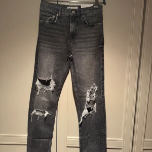 Svarta slim fit straightleg jeans med slitningar - Säljer ett par gråsvarta jeans från Zara med slim fit straight leg med flera slitningar på. Modellen är high waist och full längd, med klassisk femficksdesign. Jeansen har en cool, tvättad look och är perfekta för dig som gillar en modern stil. Köpte den med glädje och gillar verkligen passformen men  har aldrig lyckats använda dem därför väljer jag att sälja dem. 