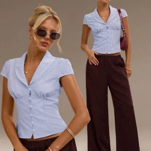 Blå vit blus topp  - Säljer en kortärmad blus med blå och vita ränder, figurnära passform och snygg krage. Blusen har knappar framtill och lätt markerad midja. Perfekt till vida byxor eller jeans för en trendig look. 🥰