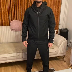 Svart vindjacka från Uniqlo - Säljer en stilren svart vindjacka från Uniqlo med hel dragkedja och praktisk huva. Jackan har en clean look, långärmade ärmar och är gjord i lätt polyester som passar perfekt för aktiva dagar. Perfekt för dig som gillar sportig och enkel stil. Bara använt den en gång.