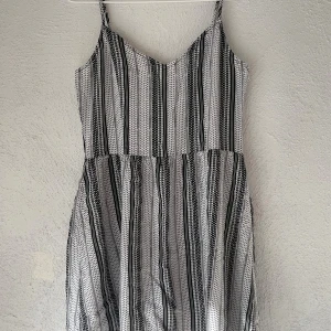 Randig sommarklänning med smala axelband - Säljer en luftig och skön kortklänning med smala axelband och v-ringad front. Klänningen har ett svartvitt randigt mönster med små prickar och ett rynkat parti i ryggen för extra komfort. Perfekt för varma dagar och enkel att styla med sneakers eller sandaler.