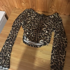Leopardmönstrad mesh topp med snörning - Säljer en långärmad mesh topp med leopardmönster i bruna och svarta toner. Toppen har offshoulder-modell och snörning framtill vid bysten. Tunt och stretchigt material som ger en cool och trendig look.