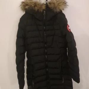 Svart dunjacka med päls från Canada Goose - Oäkta Canada Goose Jacka, i storlek S men jag skulle säga att den sitter som en XS.   Säljer en svart dunjacka från Canada Goose med fluffig päls på huvan och klassisk röd logga på ärmen. Jackan har långa ärmar, tvåvägsdragkedja och quiltad design. Perfekt för kalla vinterdagar och har en riktigt snygg siluett.