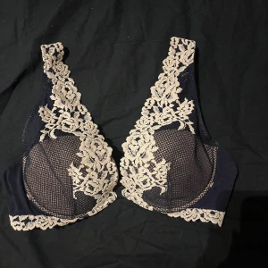 Svart spetsig korsett med blommönster - Säljer en svart korsett med ljus spets och blommigt mönster. Den har breda axelband och genomskinliga partier med detaljerad broderad spets längs kanterna. Perfekt för dig som gillar romantiska och snygga detaljer.