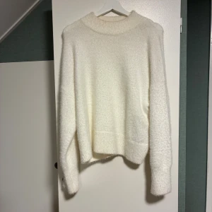 Vit fluffig stickad tröja H&M L - Supermjuk och fluffig vit stickad tröja från H&M i storlek L i fint skick. Tröjan har en bred ribbad kant nertill och vid ärmslut, samt en högre rund halsringning. Perfekt för lager-på-lager och  höst- och vintergarderoben. 