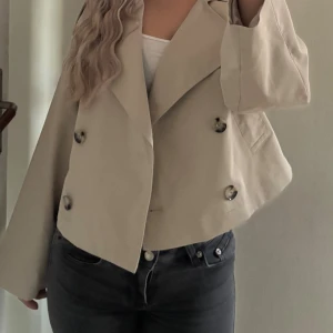 Beige trenchcoat  - Snygg croppad trenchcoat i beige med bred krage och dubbelknäppning framtill. Den har ett brännmärke innanför kappan som ej syns på utsidan. Utöver det så är den i perfekt skick med lappen kvar. Orginalpris:750kr🌸