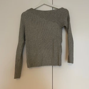 Grå ribbad offshoulder tröja - Snygg grå långärmad tröja med ribbad struktur och offshoulder-design. Tröjan har en asymmetrisk halsringning som ger en cool och modern vibe. Perfekt för dig som gillar stilrena och enkla plagg med en twist. Mjuk och skön kvalitet.