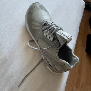 Grå adidas sneakers med snörning - Snygga grå sneakers från adidas med klassisk logga på plösen och innersulan. Skon har en rund tå, platt sula och detaljer i syntetmaterial samt textil. Stilren design med grå nyanser och snörning framtill. Perfekt för dig som gillar sportig och clean look. Nästa intill oanvända 