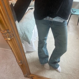 Blå bootcut jeans med råa kanter - Säljer ett par blå jeans med bootcut passform och råa, slitna kanter längs benen. Jeansen har klassisk femficksdesign och är tillverkade i ett robust denimtyg. Perfekta för dig som gillar en avslappnad och trendig stil.