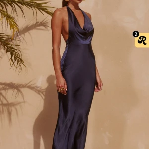 Marinblå långklänning i satin - Säljer min balklänning som är en marinblå långklänning i satin med halterneck och öppen rygg. Klänningen har en snygg draperad urringning och knyt i nacken. Den sitter figurnära och har en elegant, glansig finish som ger en lyxig känsla. Perfekt för bal.