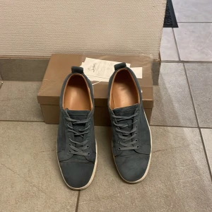 Mörkblå mocka sneakers från Louboutin - Snygga mörkblå sneakers i mocka från Louboutin med klassisk röd sula och vita kanter. Skorna har rund tå, snörning och en stilren design med ljusbrunt skinnfoder. Perfekt för dig som gillar exklusiva detaljer och vill sticka ut med röd undersida.kvitto finns.