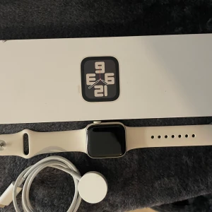 Apple Watch SE GPS 40 mm stjärnglans alum, stjärnglans sportband-s/m - Säljer en   Apple Watch SE GPS 40 med vit silikonarmband och fyrkantig skärm. Klockan har en modern design och kommer med originalförpackning samt laddare. Perfekt för dig som vill ha koll på tiden och dina aktiviteter direkt på handleden. Pris kan diskuteras