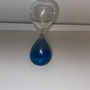 Timglas med blått sand - Elegant timglas i glas med blått sand. Perfekt som dekor eller för tidtagning vid spel och aktiviteter. Produkten ser ut att vara i mycket gott skick utan synliga repor eller skador.