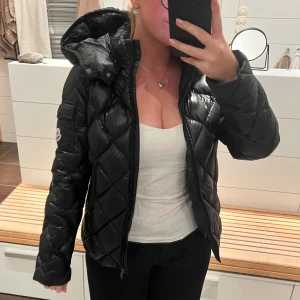 Svart Moncler Jacka - Jättefin svart Moncler lite tjockare dunjacka. Två fickor med dragkedjor, dragkedja för att knäppa jackan, stor luva, knappar så man kan ta av luvan. Ficka med Moncler märket på vänster arm. Väldigt bra skick passar storlek XS eller också stor flicka alltså storlek 170. Jag har massa fler bilder så bara att be om det. Och bilder på alla märken på insidan självklart men går bara att lägga 5 bilder. 