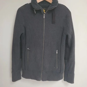 Mörkgrå teddyjacka/kofta från Selected - Mörkgrå teddyjacka från Selected med ribbad utsida och mjukt teddyfoder. Jackan har dragkedja framtill, två fickor med dragkedja och hög krage med snörning. Perfekt för kalla dagar och har en clean, modern look. jackan är i storlek M men skulle passa till S Priset går alltid att diskutera hör av er om ni har frågor eller om ni undrar över något 😊