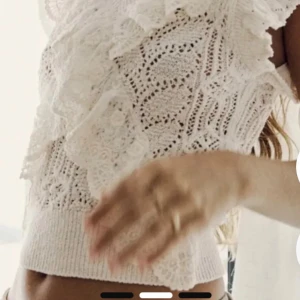 Vit spetsig blus med volang - Superfin vit blus med bred volangkrage och spetsdetaljer. Blusen är stickad med ett mönstrat hålmönster och har korta ärmar. Den är croppad och har en romantisk vibe, perfekt för dig som gillar detaljer och ljusa färger.